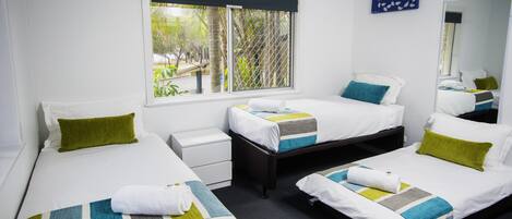 A hotel room with two single beds, a small bedside table, a large window with a view of greenery, and a mirror on the wall.