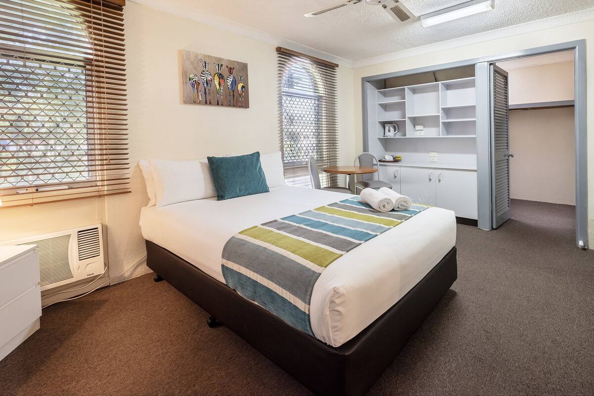 Habitación de hotel ordenada con cama, escritorio, silla y armario.