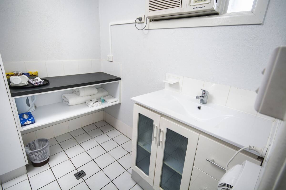 Un baño pequeño y limpio con un lavamanos blanco, un perchero, un espejo y una unidad de ventilación sobre el lavamanos.