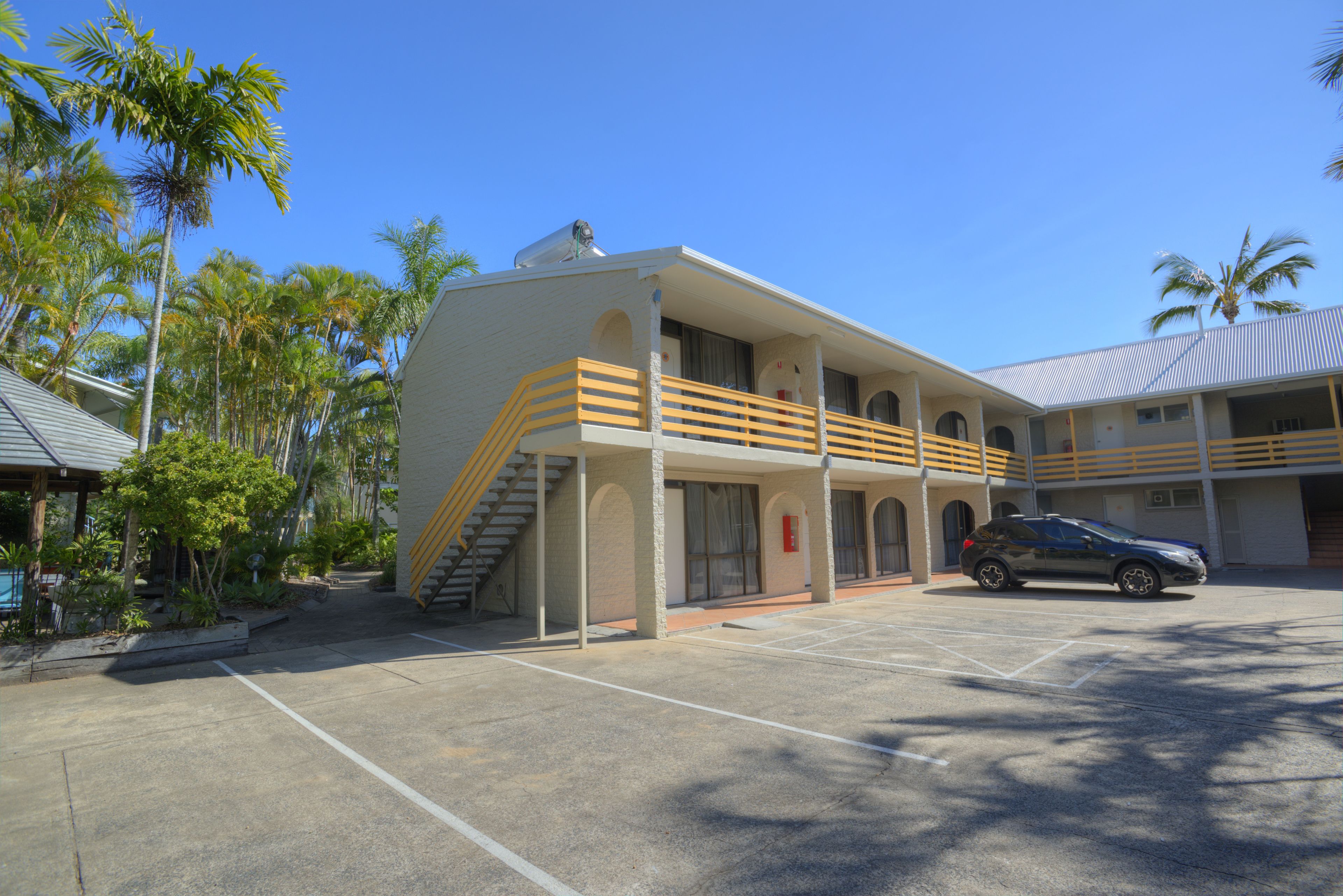 Un bâtiment à deux étages avec un parking, un escalier et une voiture garée devant.