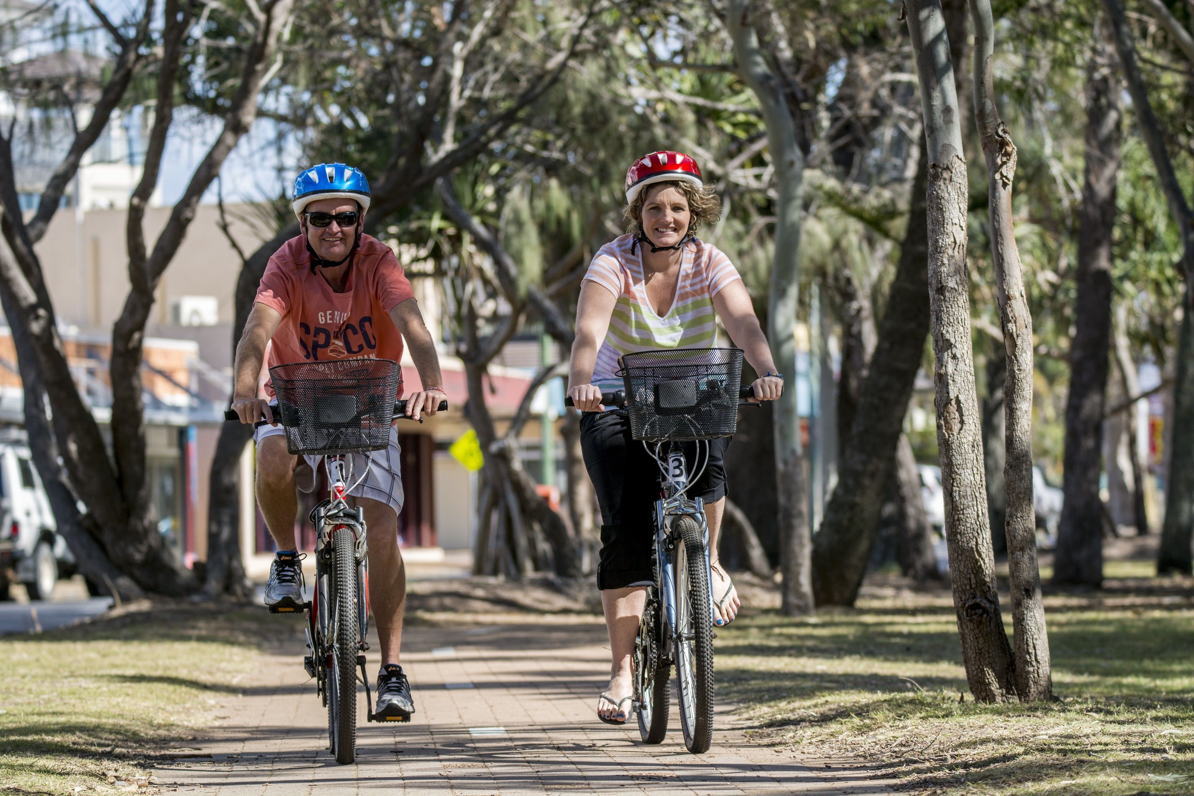 Dos personas paseando en bicicleta por un camino pavimentado rodeado de árboles.