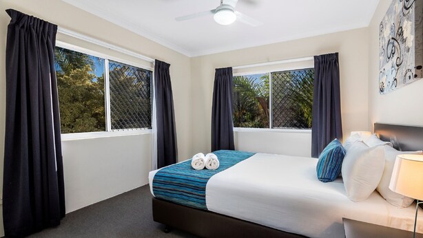 A hotel room with a bed, two windows with curtains, a ceiling fan, and a wall with artwork. - The Beach Motel Hervey Bay (Torquay)