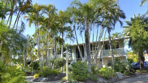 A hotel with a paved walkway, palm trees, and a building with balconies. - The Beach Motel Hervey Bay (Torquay)