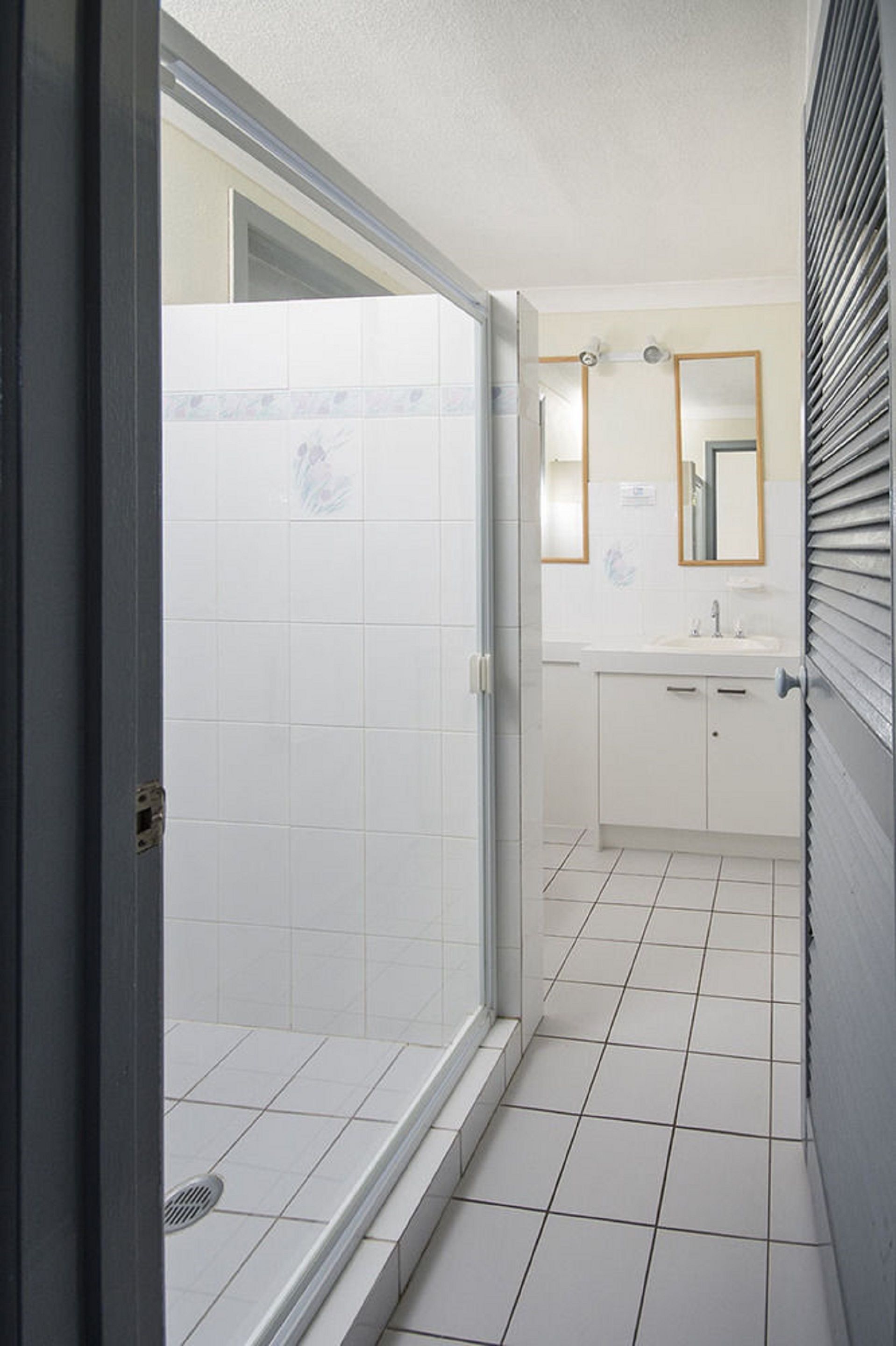 Un baño con azulejos blancos, ducha, lavabo y espejo.