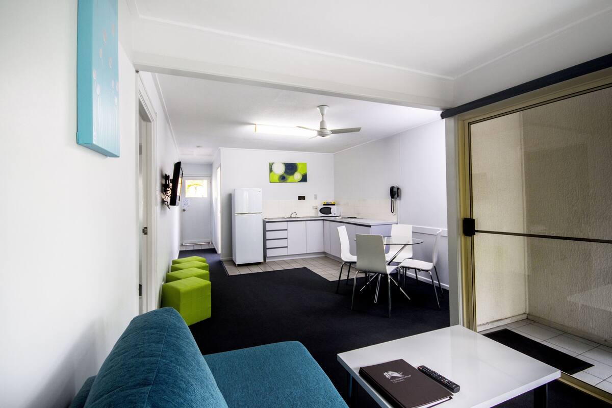 Un espacio habitable compacto con kitchenette, zona de comedor y área de estar con sofá y mesa.