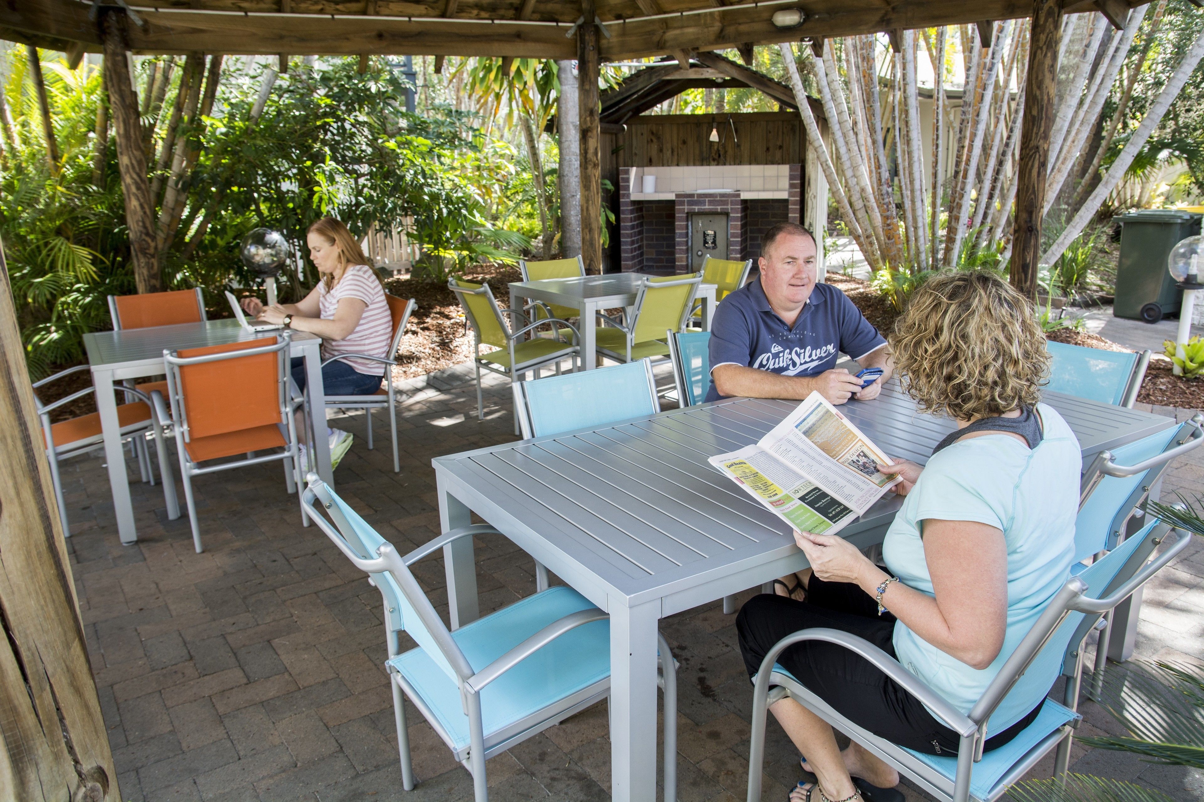 An outdoor patio area with metal tables and chairs, surrounded by greenery.
