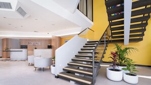 A modern hotel lobby with a staircase, reception desk, and potted plants. - Mercure Rockhampton (Rockhampton)