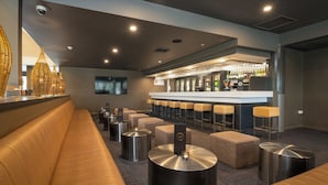 A modern bar area with a long bench seating, a bar counter with stools, and a variety of bar accessories. - Mercure Rockhampton (Rockhampton)
