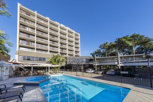 Un hotel con piscina, mobiliario exterior y un edificio de varios pisos.