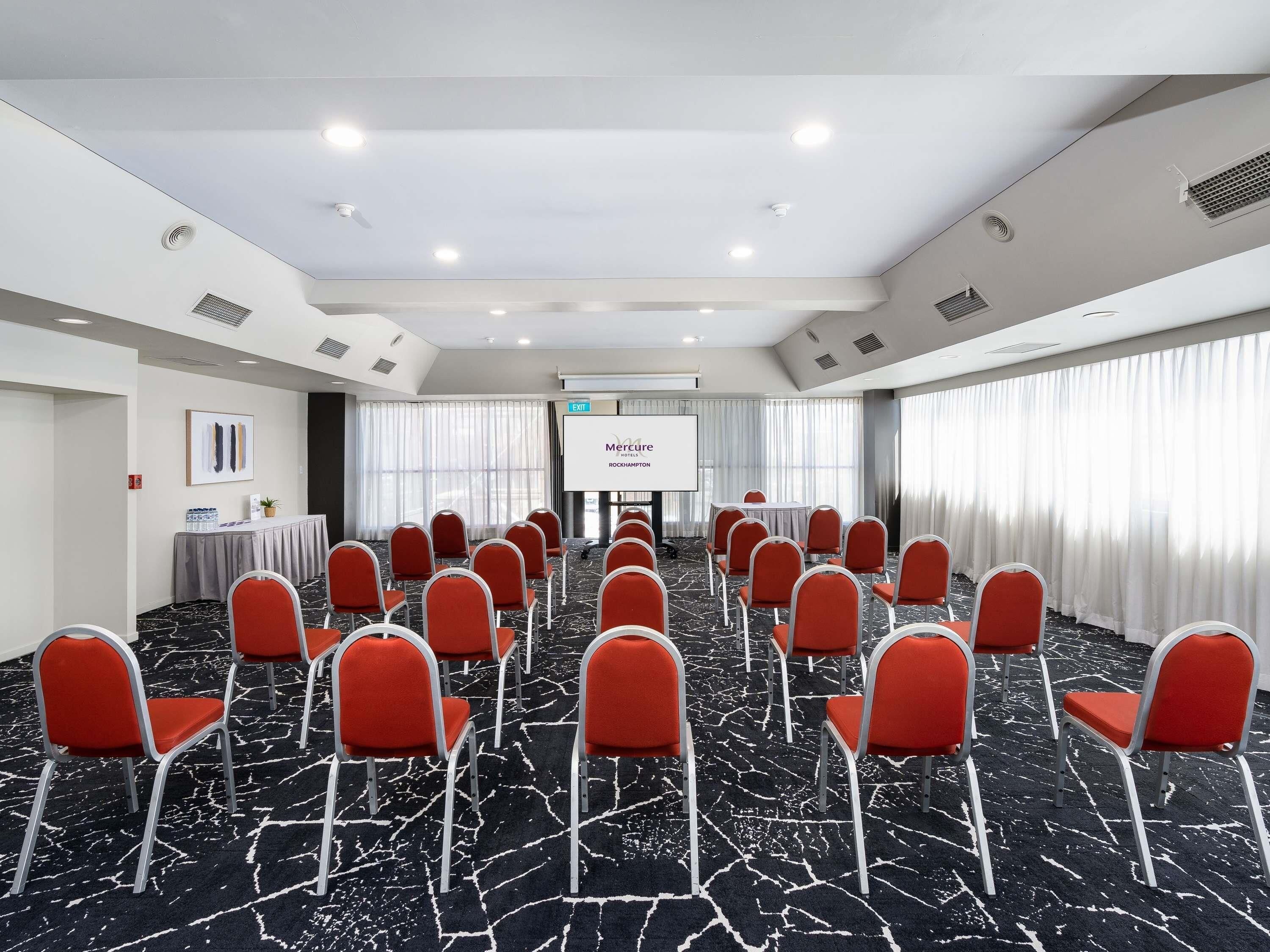 A conference room with rows of red chairs, a projector screen, and a presentation on the wall.