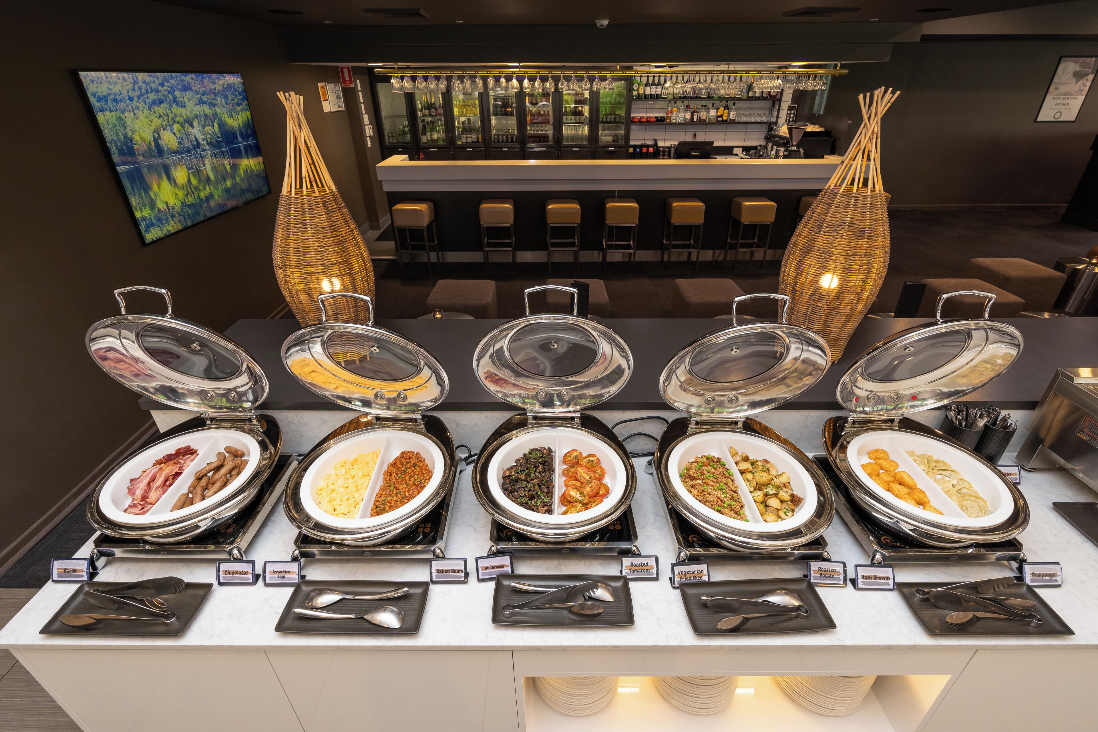 Un buffet avec des présentoirs indiquant les différents types de plats, un bar et un espace détente avec des chaises.
