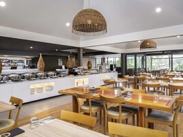 Un restaurante moderno con mesas y sillas de madera, una zona de bufé y grandes ventanales con vistas al exterior.