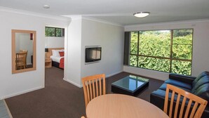 A modern hotel room with a dining area, a sofa, a TV, and a large window with a view of greenery. - Comfort Inn Grammar View (East Toowoomba)