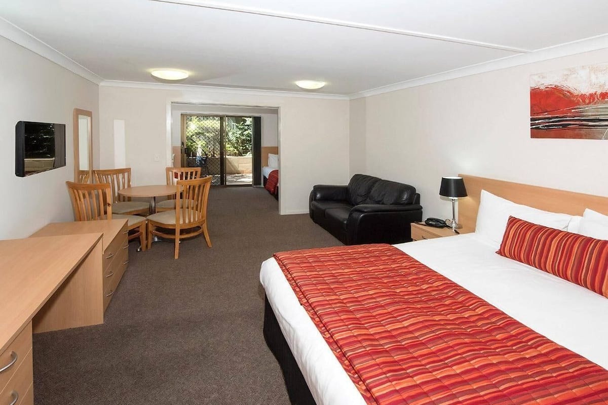A hotel room with a bed, a desk, a chair, a couch, and a door leading to a balcony.
