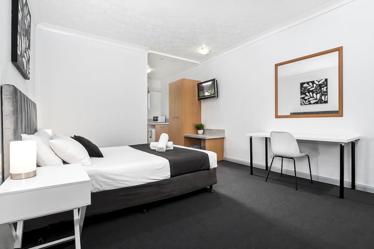 A hotel room with a bed, bedside table, desk, chair, TV, and artwork.