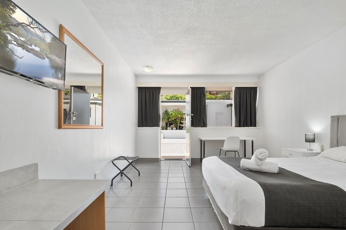 A modern hotel room with a bed, desk, chair, and a TV mounted on the wall.
