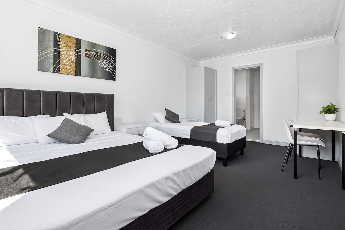 A modern hotel room with two beds, a desk, and a chair.