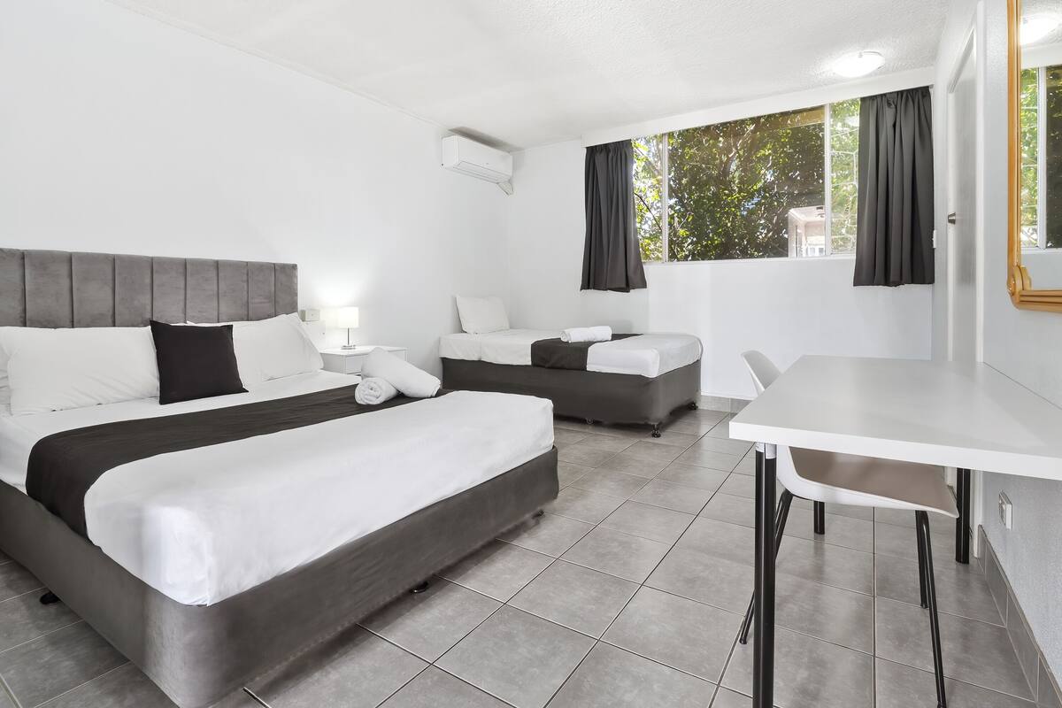 A hotel room with two beds, a dining table, and a window with curtains.