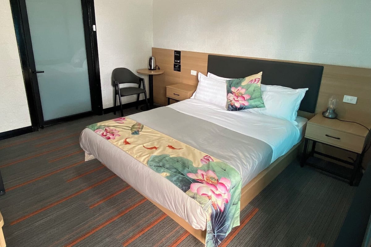 A hotel room with a bed, a chair, a small table, and a nightstand.