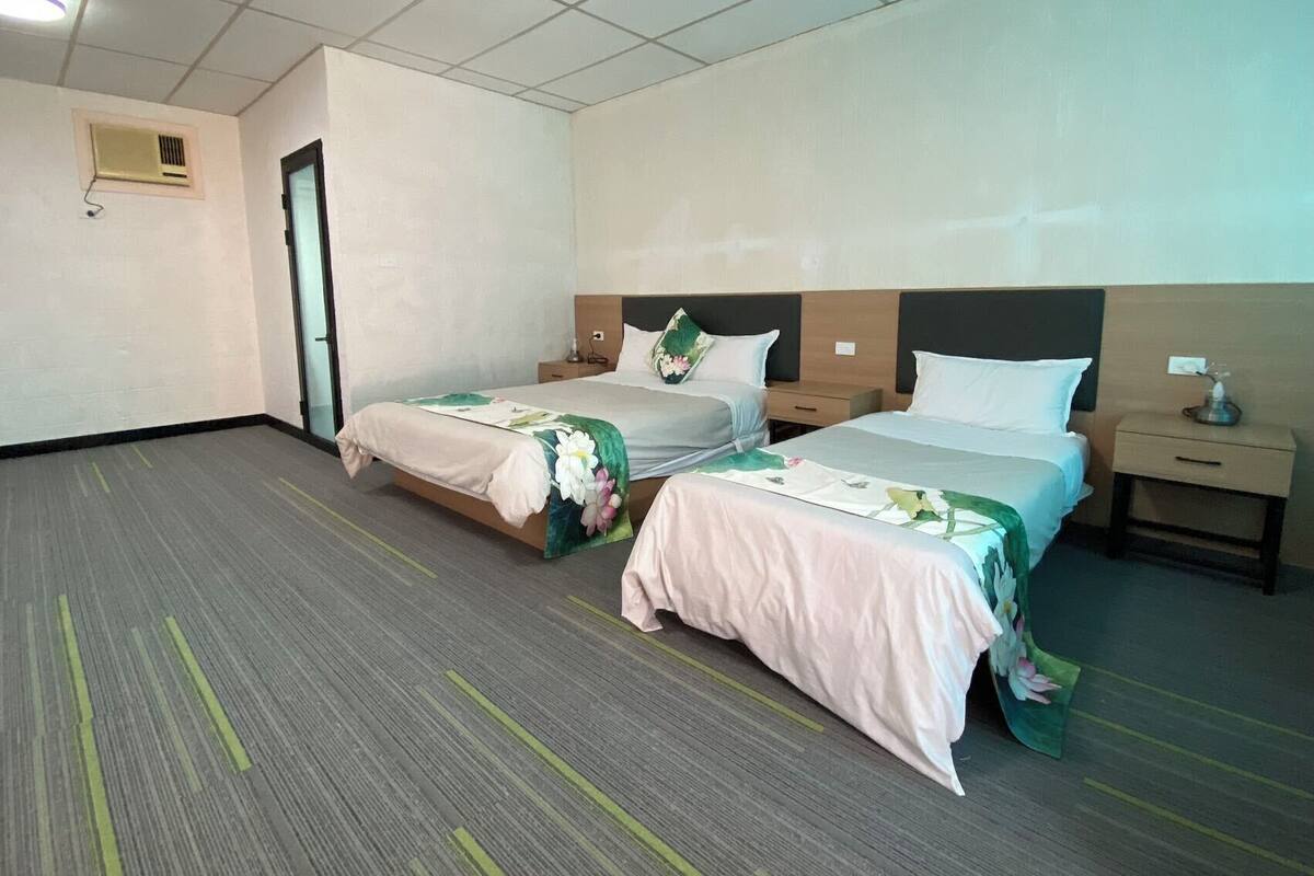 A hotel room with two beds, a small desk, a chair, and a window.