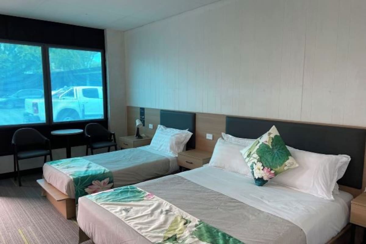 A hotel room with two beds, a large window, a desk, and chairs.