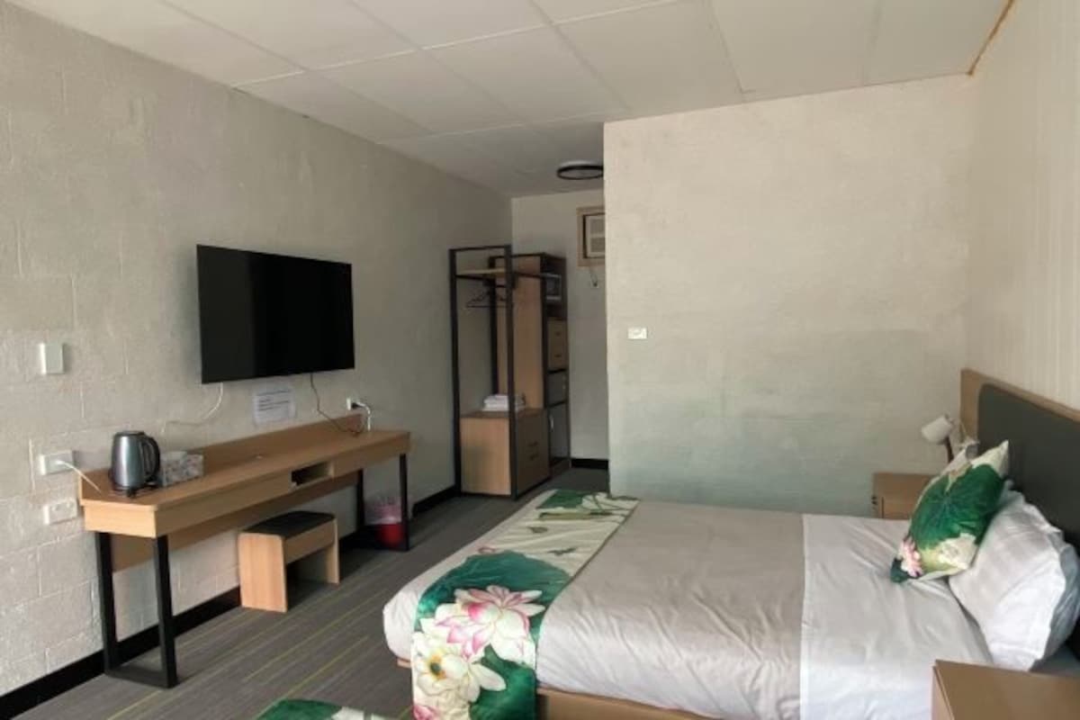 A hotel room with a bed, a TV mounted on the wall, a wooden desk, and a wardrobe.