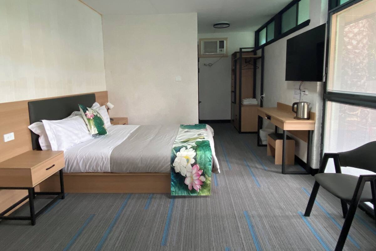 A hotel room with a bed, a desk, a chair, and a TV.
