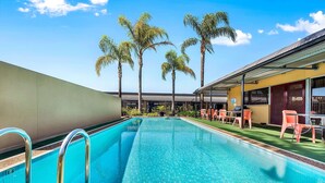 A swimming pool with clear blue water, surrounded by palm trees and outdoor seating. - Comfort Inn & Suites Manhattan (Enfield)
