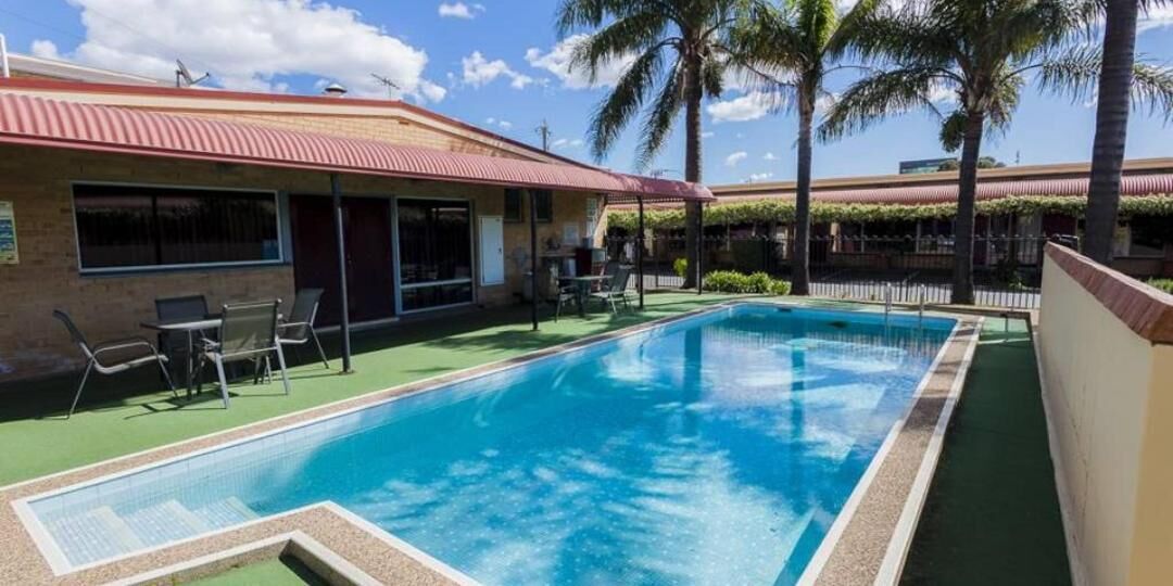 A swimming pool with lounge chairs and a building with a red roof.