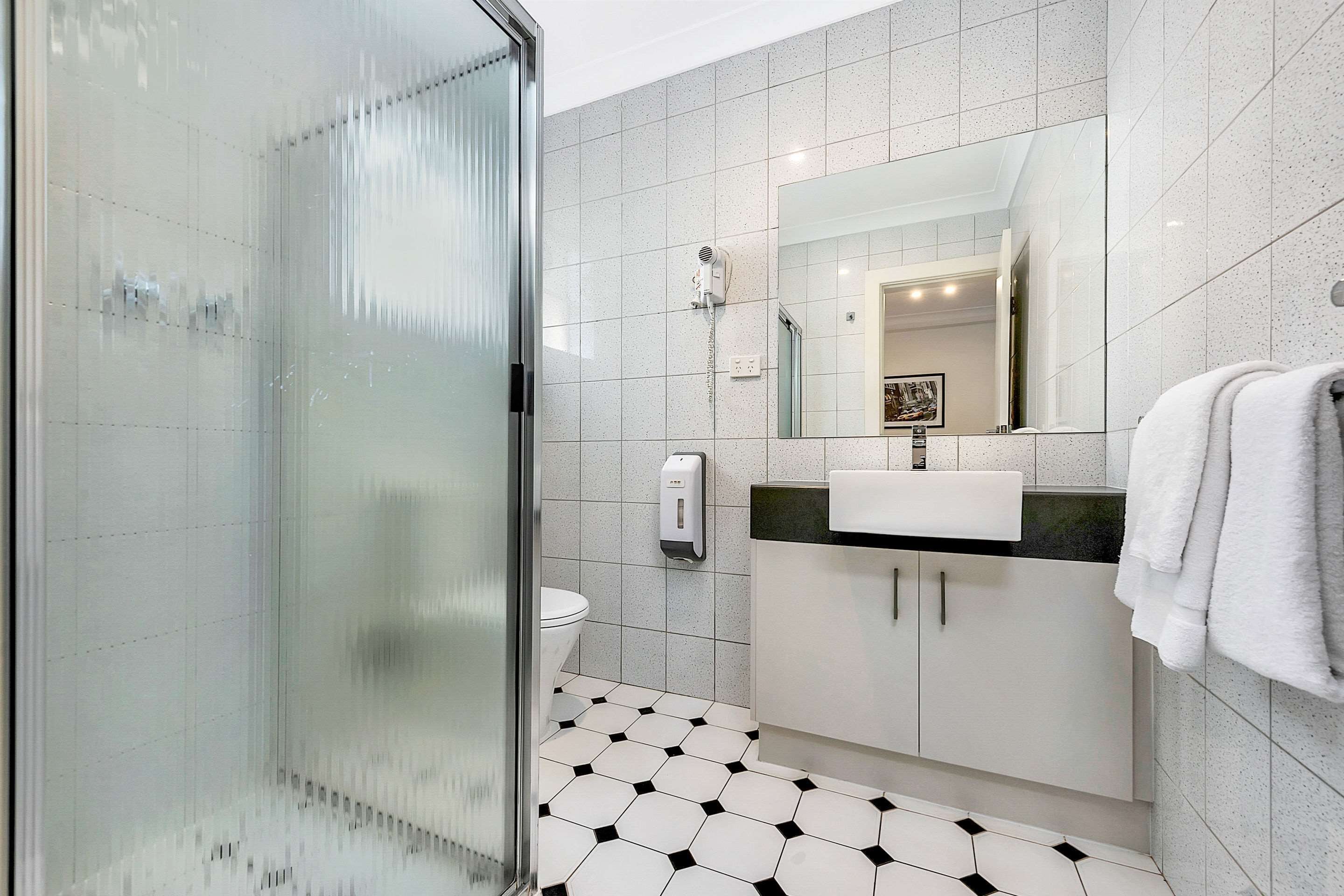 Un baño moderno con cabina de ducha de vidrio, inodoro, lavabo con espejo y toallero.