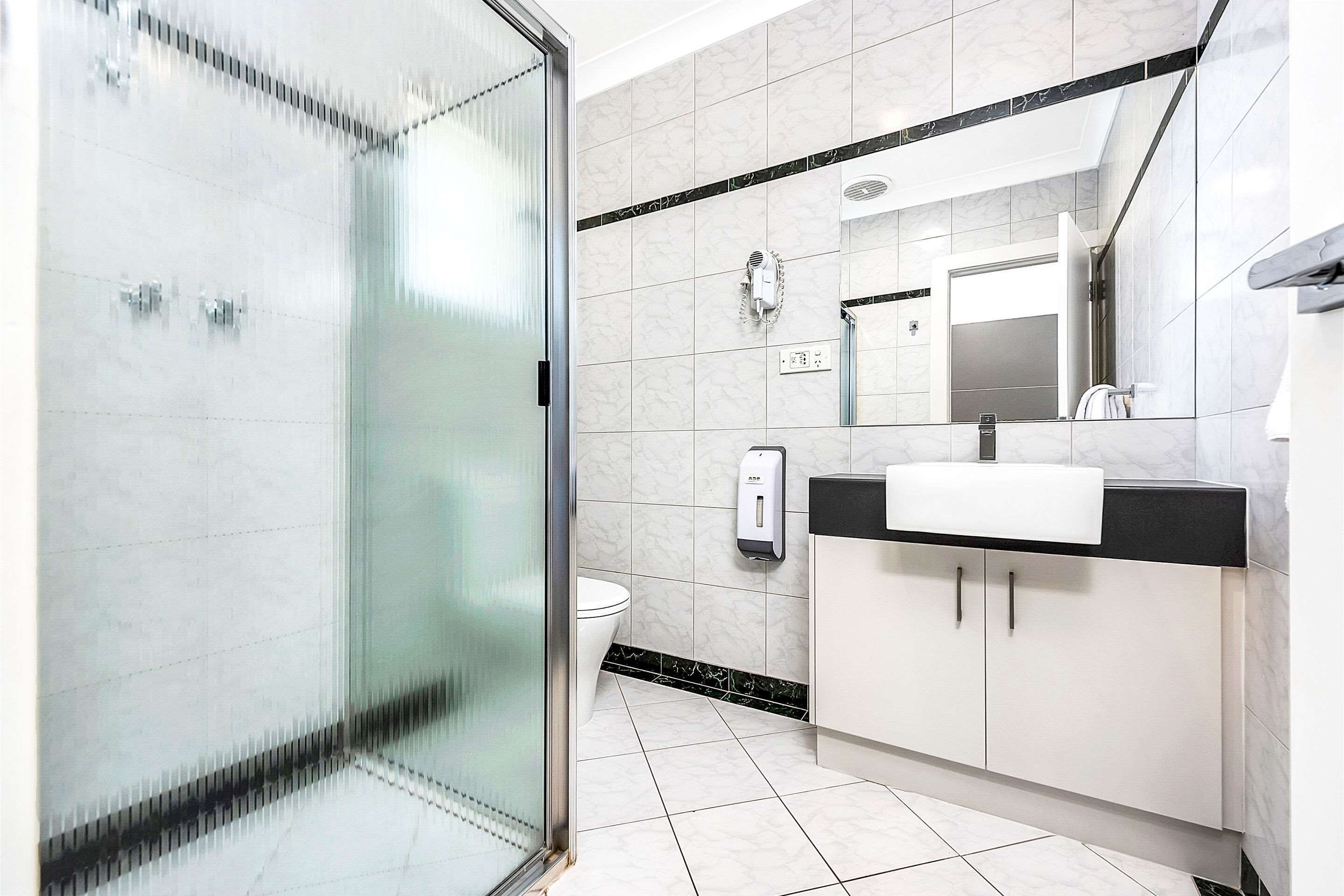 A modern bathroom with a glass shower enclosure, a white toilet, a black and white vanity, and a large mirror above the sink.