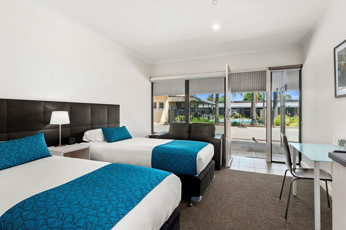 A hotel room with two beds, a desk, and a view of the outside.