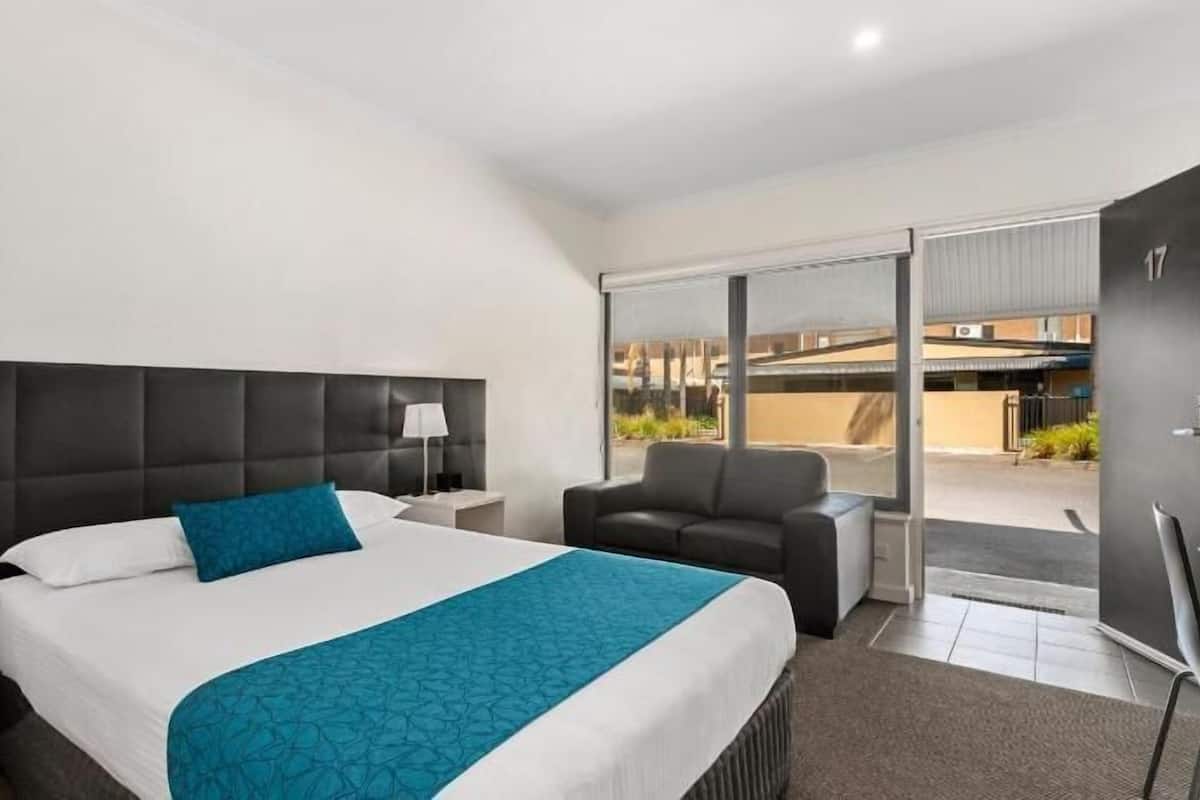 A hotel room with a bed, a nightstand, a chair, a desk, and a large window.