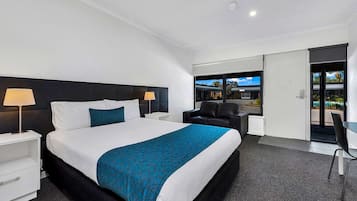 Habitación de hotel con una cama grande, dos mesitas de noche con lámparas, un sofá negro, un escritorio y vistas al exterior a través de una puerta corredera.