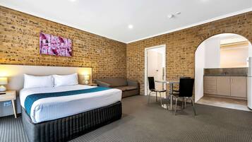 Una habitación de hotel con pared de ladrillo, una cama, un sofá, una pequeña mesa con sillas y una kitchenette.