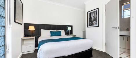 A modern hotel room with a large bed, a nightstand, a bedside table, and a door leading to a bathroom.