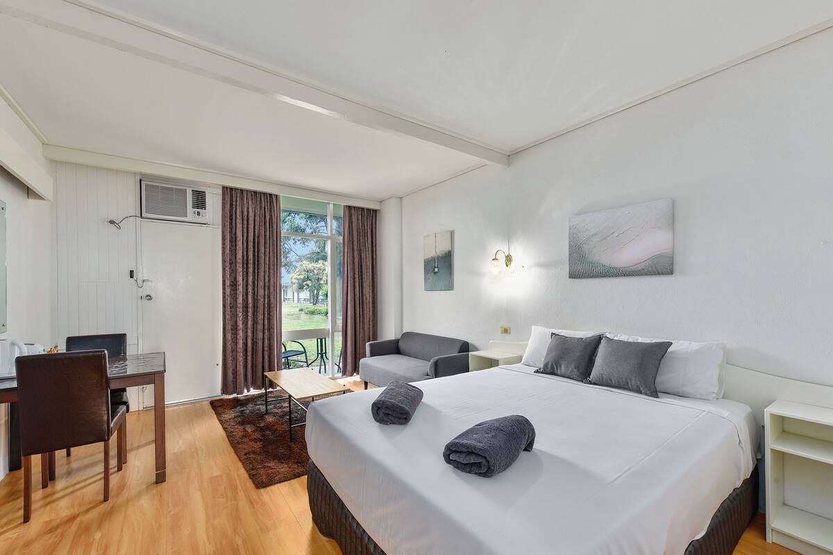 Une chambre d’hôtel équipée d’un lit, d’un bureau, d’une chaise, d’une petite table et offrant une vue sur l’extérieur.