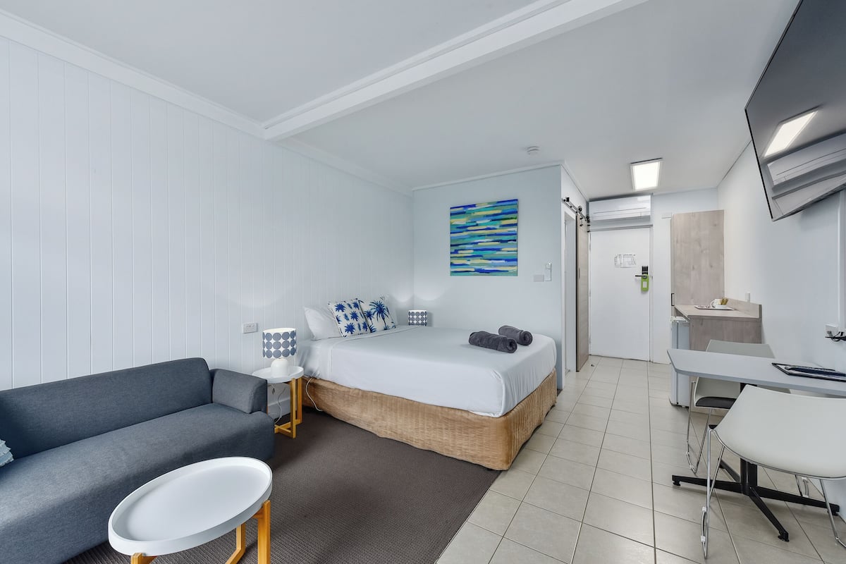 Une chambre d’hôtel moderne équipée d’un lit, d’un canapé, d’une petite table, d’une télévision et d’un bureau avec des chaises.