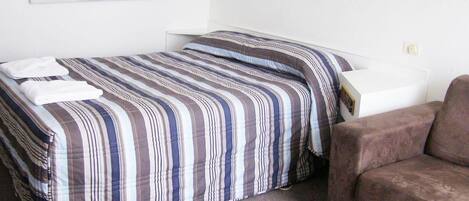 Una habitación pequeña y ordenada con una cama individual, un sofá y una mesita.