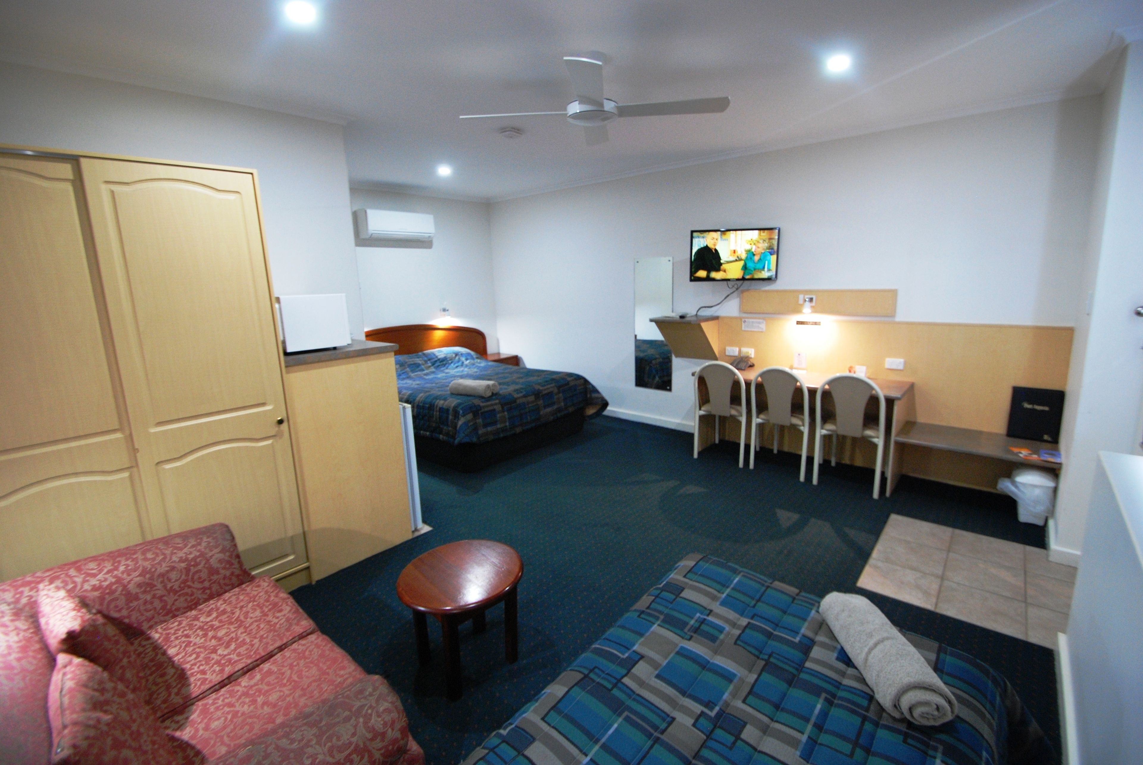 A hotel room with a bed, a desk with a chair, a television, and a wardrobe.