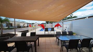 An outdoor patio area with a table and chairs, a pool in the background, and a covered seating area.