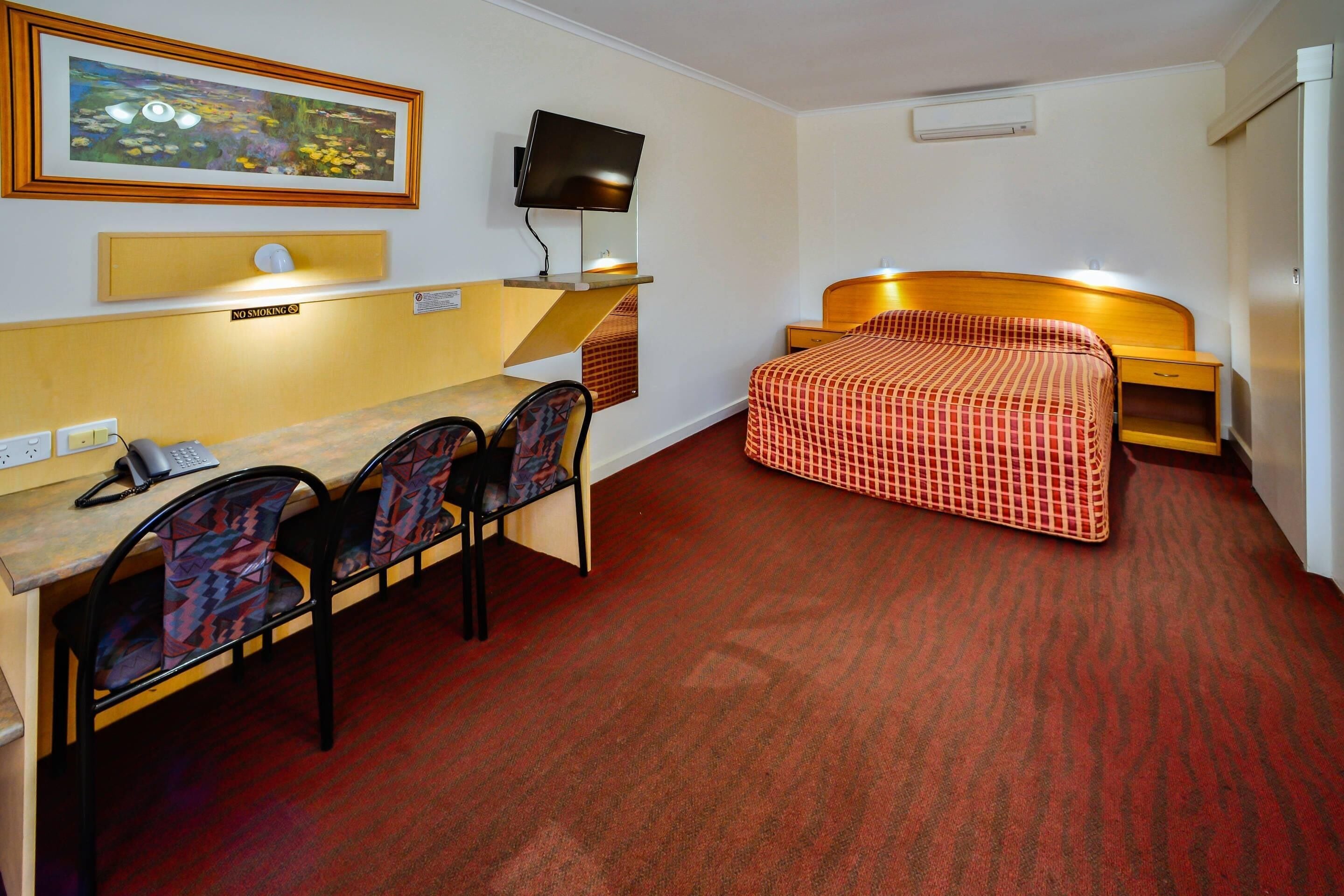 A hotel room with a bed, a desk, a chair, a television, and a painting on the wall.