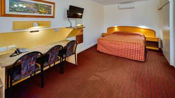A hotel room with a bed, a desk, a chair, a television, and a painting on the wall.