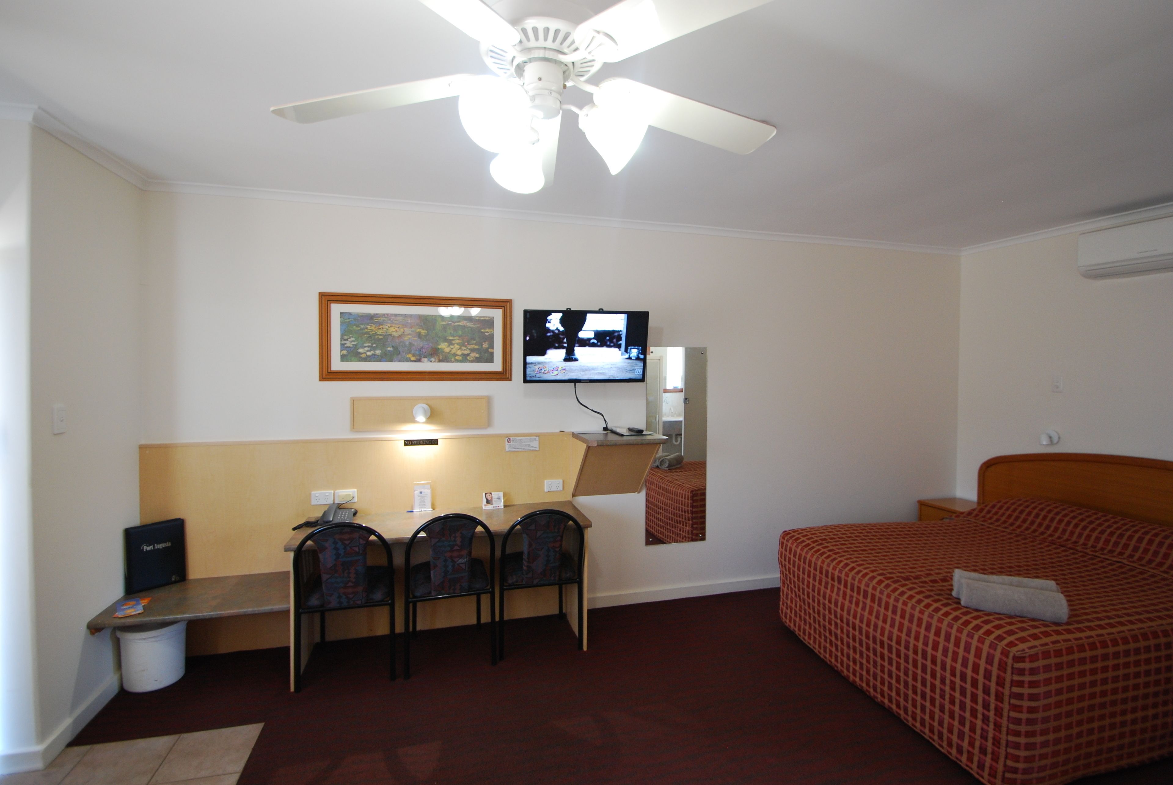 A hotel room with a bed, a desk with two chairs, a television, and a ceiling fan.