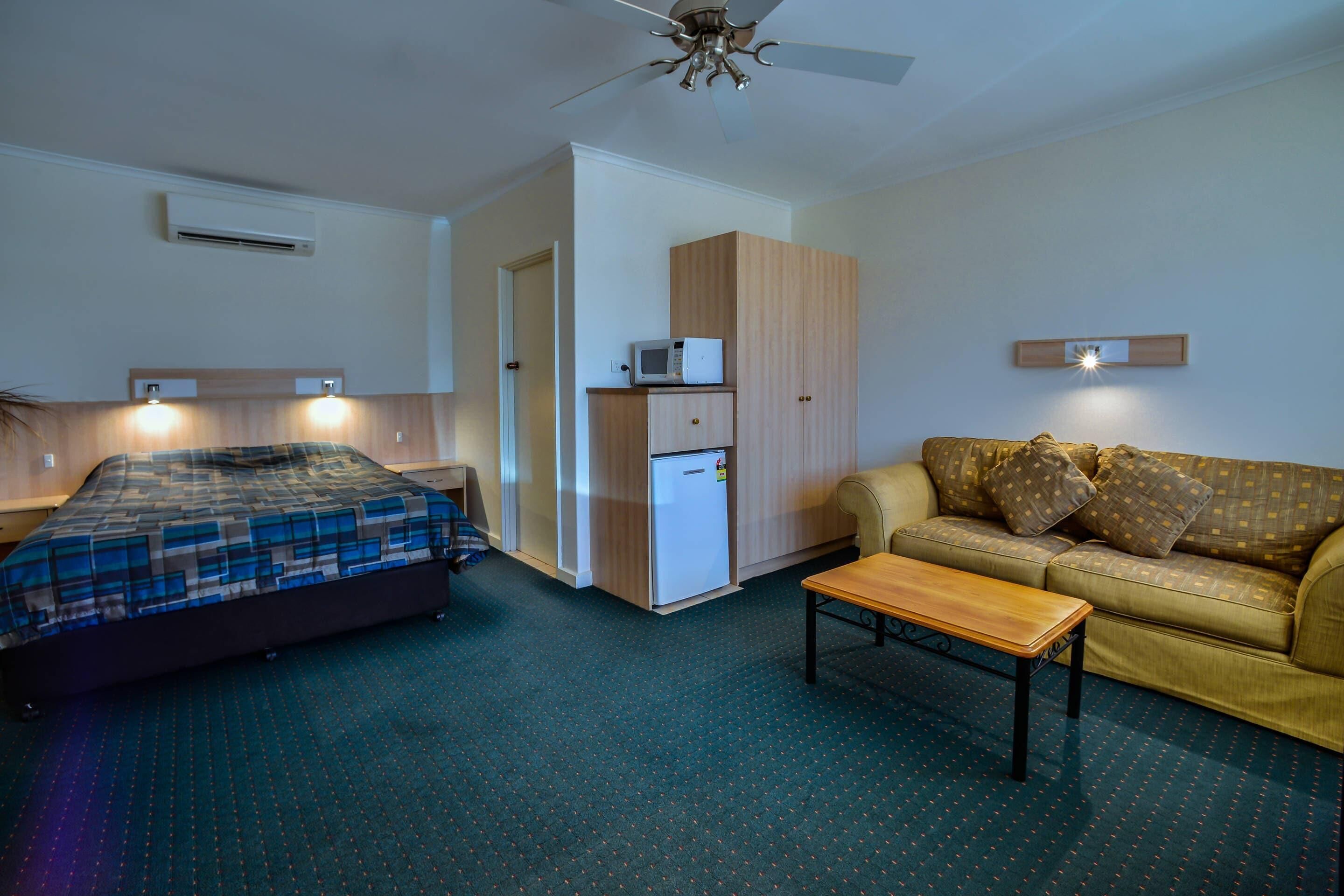 A hotel room with a bed, a sofa, a small table, a microwave, and a ceiling fan.