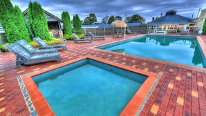 A swimming pool with two separate sections, surrounded by a red and orange tiled deck. - Bairnsdale Motor Inn (Bairnsdale)