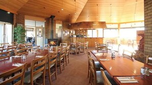 A restaurant with wooden tables and chairs, a brick wall, and a large window. - Bairnsdale Motor Inn (Bairnsdale)