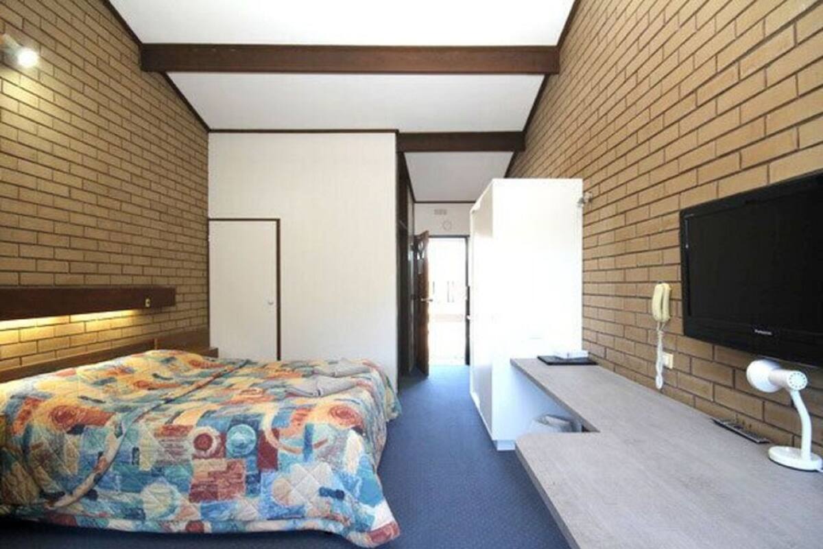 Ein Hotelzimmer mit einem Bett, einem Schreibtisch, einem Fernseher und einem Telefon an der Wand.