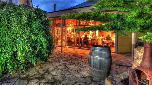 An outdoor dining area with stone paving, a large metal barrel, and lush greenery. - Bairnsdale Motor Inn (Bairnsdale)