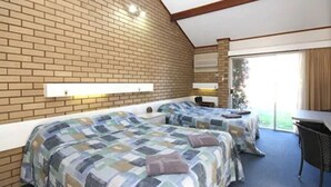 A bedroom with two beds, a brick wall, a window, and a desk. - Bairnsdale Motor Inn (Bairnsdale)